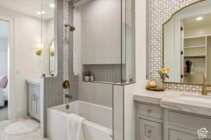 Bathtub with a glass shower panel, tiled shower niche, light-toned wood-finish flooring, vanity with a stone countertop, and an ornate framed mirror