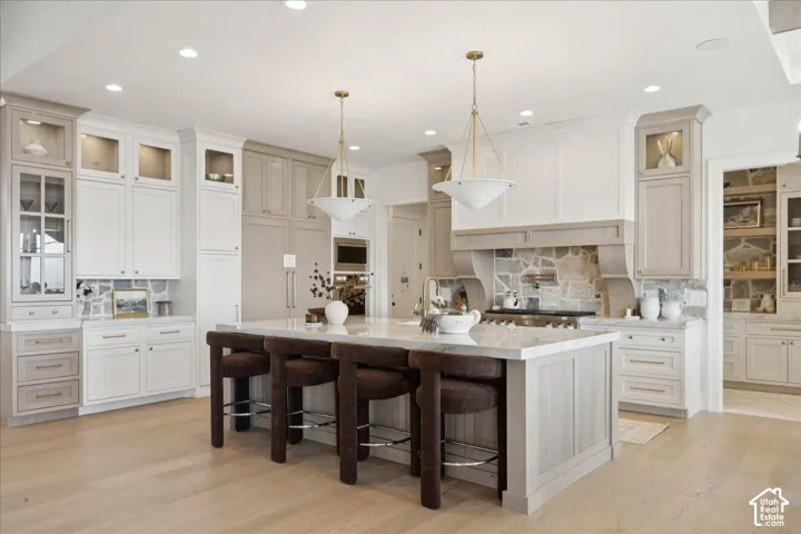 Expansive kitchen island with seating, integrated built-in appliances, stone backsplash, recessed lighting, and light wood-finish flooring