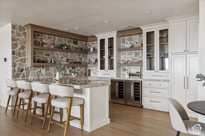 Spacious kitchen island with countertop seating, stone accent wall, custom built-in cabinetry, and integrated beverage refrigerators