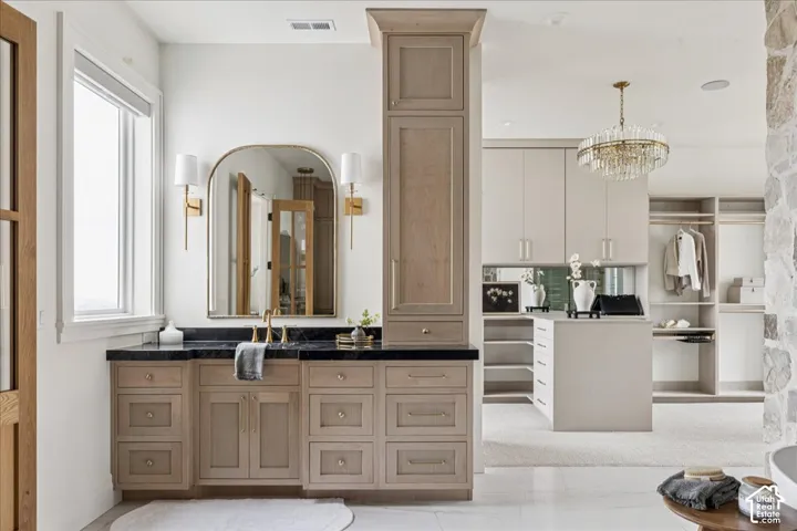 Custom vanity with dark countertop, arched mirror, and brass sconces