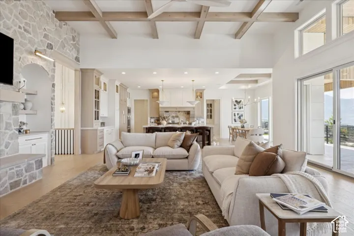 Spacious living area featuring a stone accent wall, exposed ceiling beams, wood-finish flooring, and large sliding glass doors