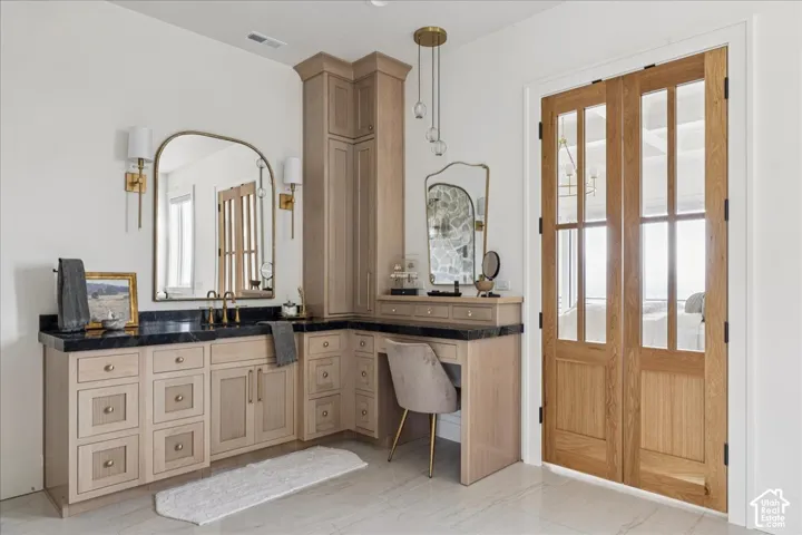 Light wood-finish cabinetry, dark countertop, and an arched mirror with sconce lighting