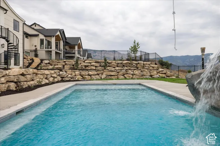 Rectangular swimming pool with concrete surround and rock waterfall feature