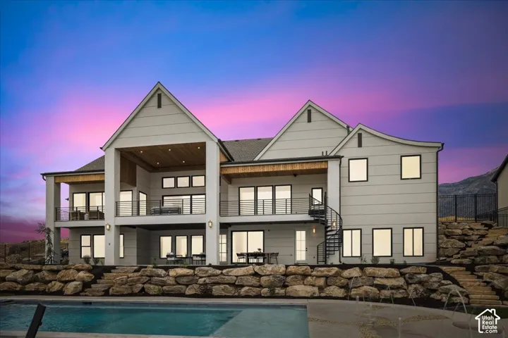 Multi-level exterior with multiple balconies featuring black railings, an outdoor pool, stone retaining walls, and a spiral staircase