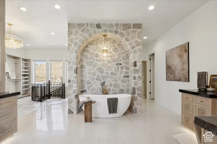 Freestanding tub set within a stone-clad alcove with an arched opening, illuminated by a pendant light