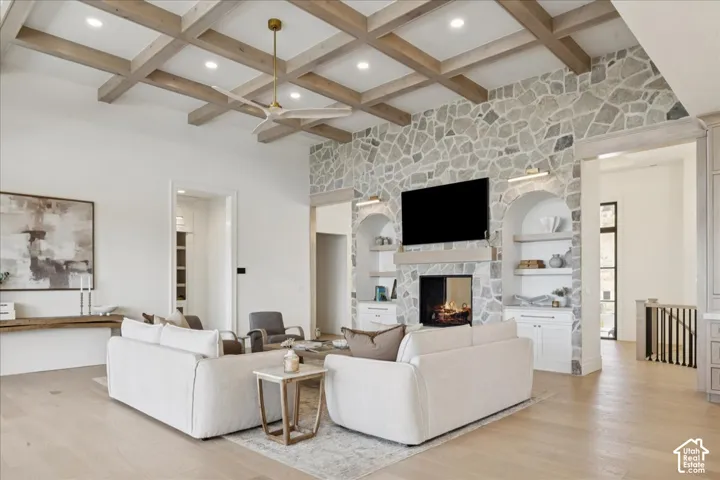Stone-clad fireplace with a wood mantel, coffered ceiling with recessed lighting, and light wood-finish flooring