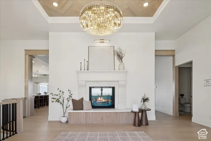 Herringbone wood-finish ceiling accent, large crystal chandelier, integrated fireplace, built-in fireplace bench with slatted wood-finish detailing, and light wood-finish flooring