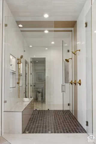 Spacious shower enclosure with glass panels, dual shower heads with brass fixtures, built-in bench, and patterned floor tiling