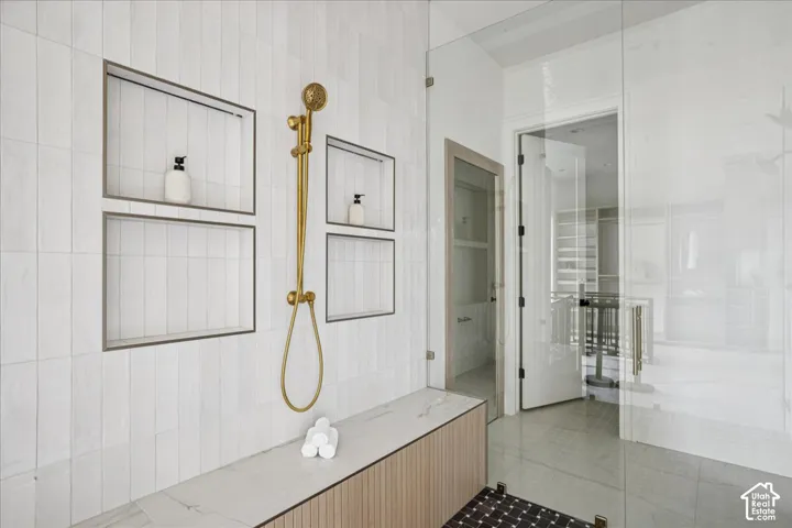Glass-enclosed shower with a gold-tone shower fixture, multiple recessed shelving niches, a built-in shower bench with a slatted wood-finish base, and vertical-stacked tile
