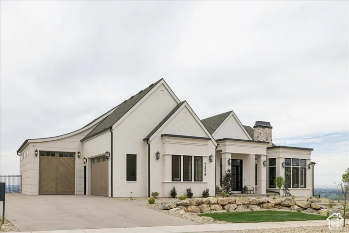 White brick exterior with dark trim windows, multi-pitch roofline, and stone chimney