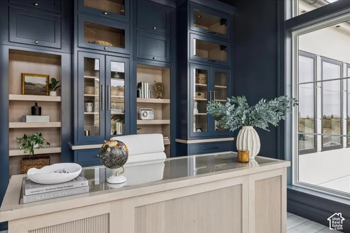 Built-in cabinetry with glass-front uppers, open shelving, and a light wood-finish desk with a glass top