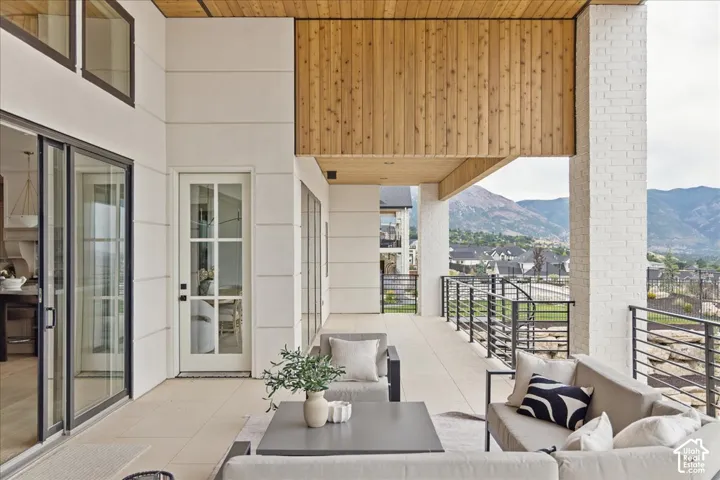 Expansive outdoor terrace with mountain backdrop, featuring a natural wood-finish ceiling, white brick accent column, and sleek metal railings