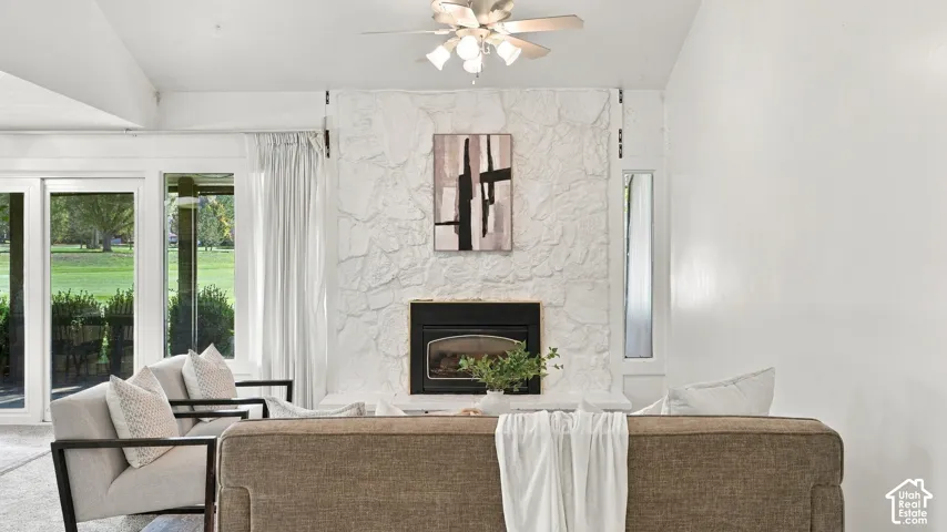 Living area featuring a stone-clad fireplace with a black insert, a ceiling fan with integrated lighting, and vaulted ceilings
