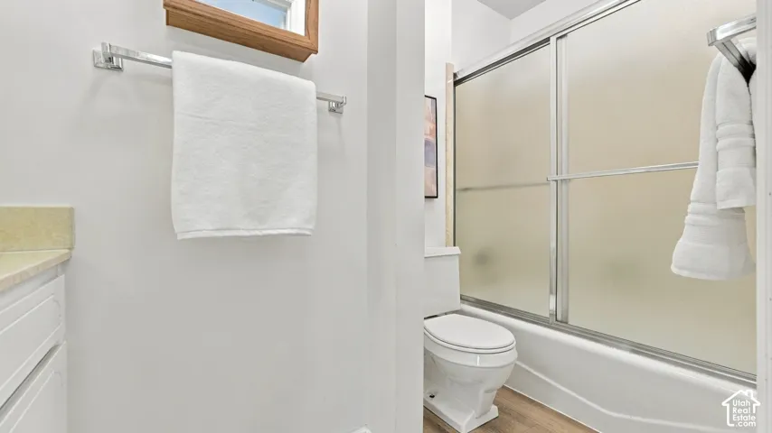 White shaker-style cabinetry with a light-toned countertop, chrome towel bar, toilet, and a shower-over-tub combination with frosted sliding doors