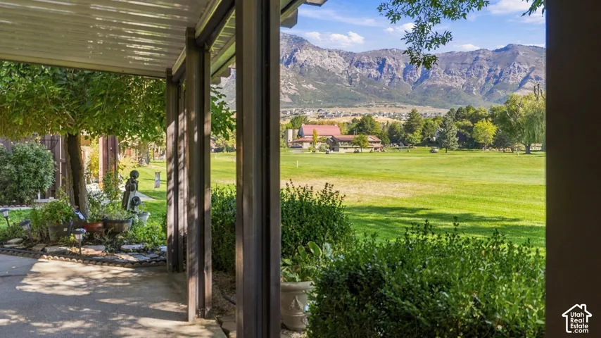Covered patio with structural columns, manicured landscaping, and a broad green expanse framed by mountains
