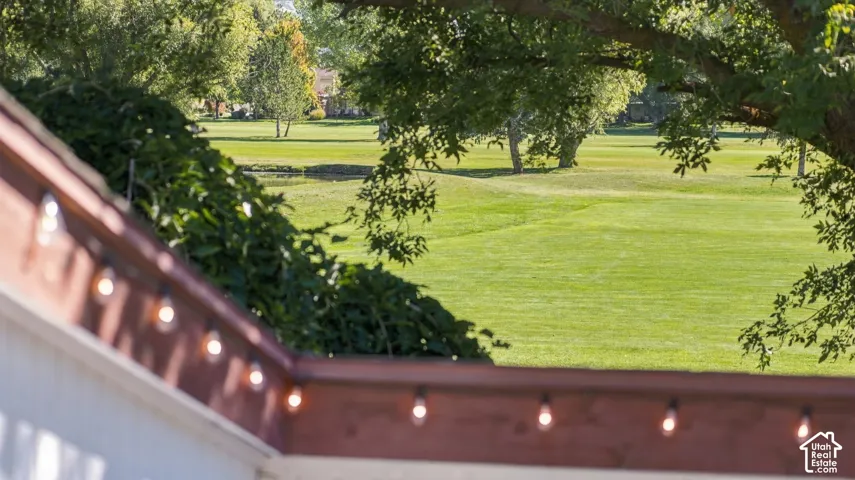 Expansive lawn with mature trees, visible from a deck featuring a wood railing and decorative string lighting
