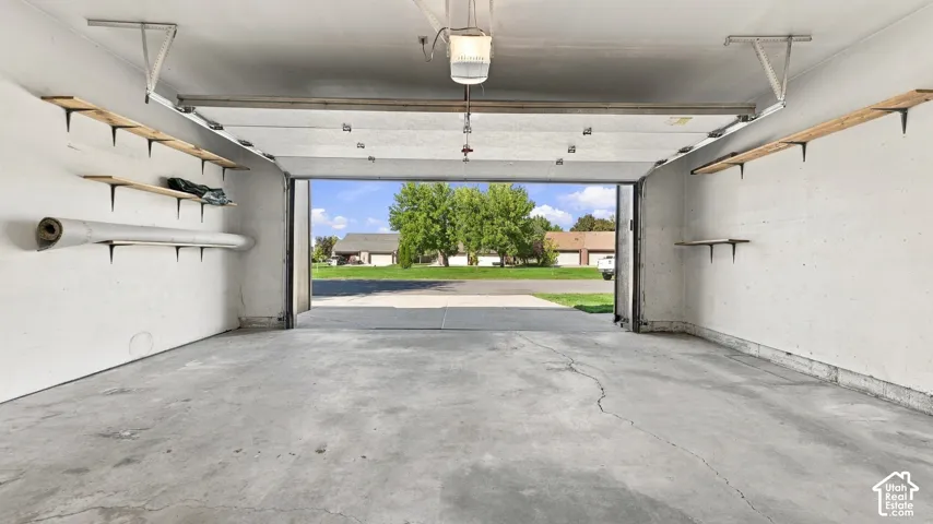 Attached garage with concrete flooring, overhead lighting, and built-in shelving