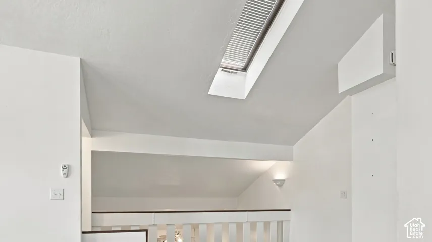 Skylight with integrated blinds, sloped ceiling, wall-mounted light fixture, and white painted railing