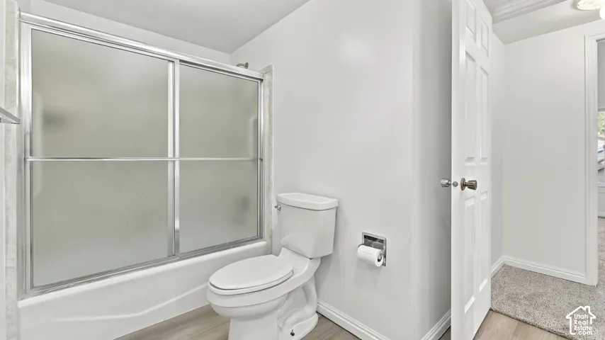 White paneled door, wood-finish flooring, and a shower-tub combination with frosted sliding doors