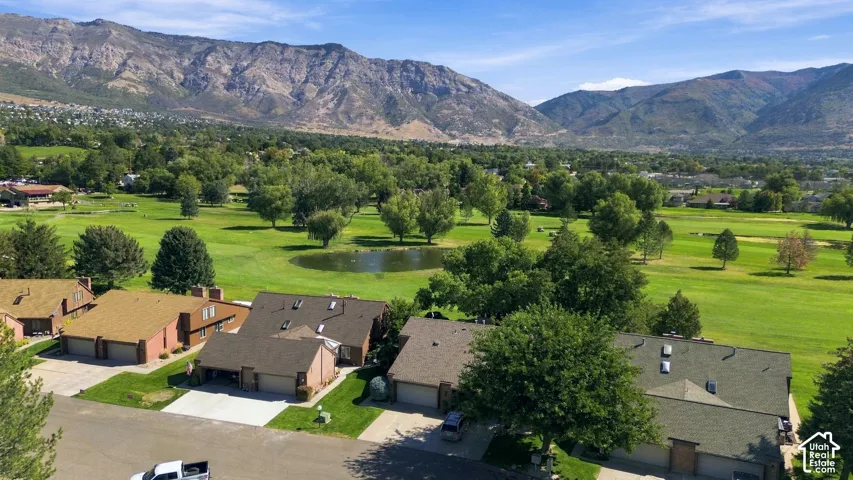 Golf course frontage with a water feature, surrounded by mature trees, and a prominent mountain range backdrop