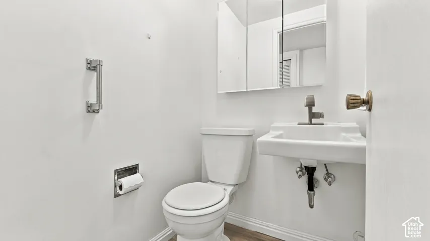 Wall-mounted sink with a single-handle faucet, medicine cabinet with mirrored doors, and wood-finish flooring
