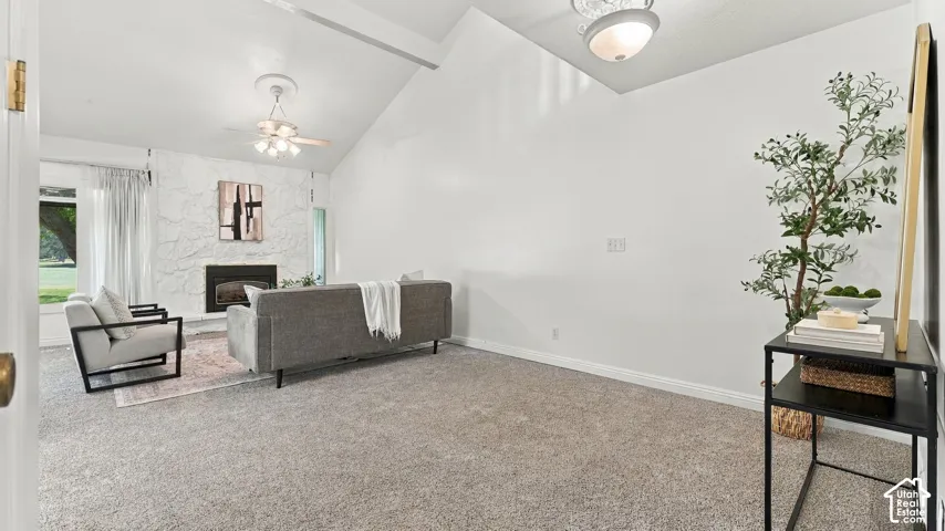 Vaulted ceiling with a ceiling fan, fireplace with a textured stone surround, large windows, and wall-to-wall carpeting