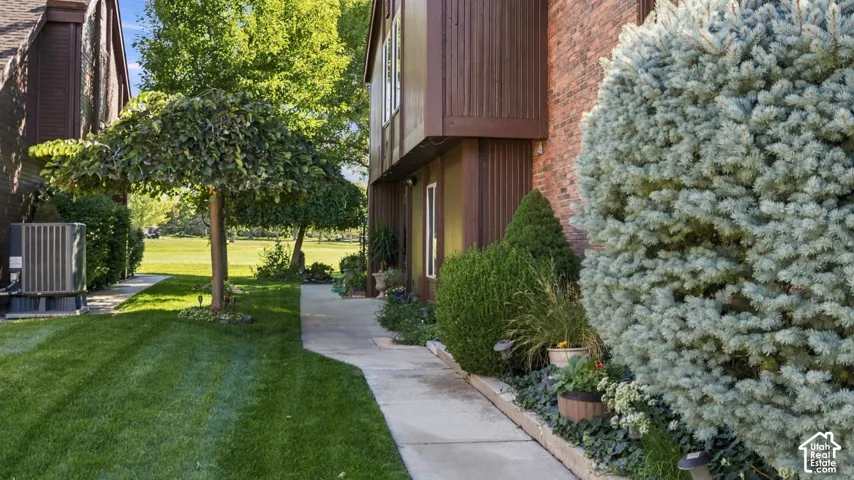 Manicured lawn, mature trees, concrete walkway, brick exterior accents, and diverse planted landscaping