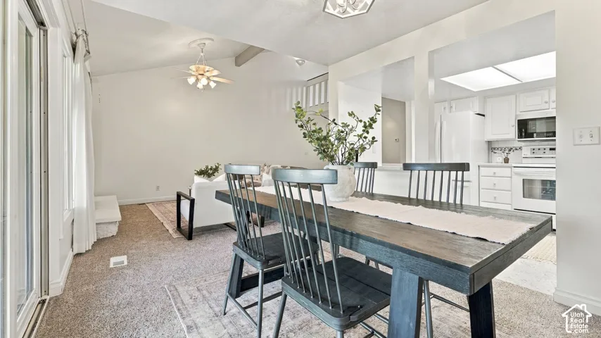 Integrated kitchen with white cabinetry and appliances, wood-finish dining table, and vaulted ceilings with a ceiling fan