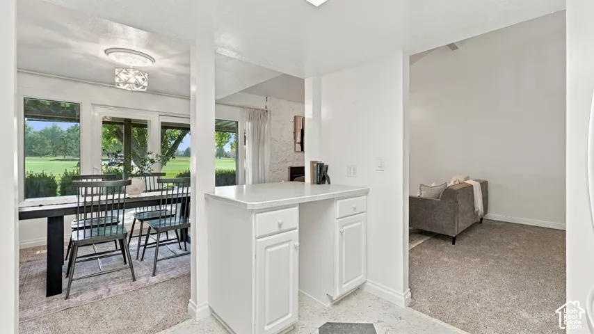 Integrated breakfast bar with white cabinetry, bright dining area with large windows, and a decorative ceiling light fixture