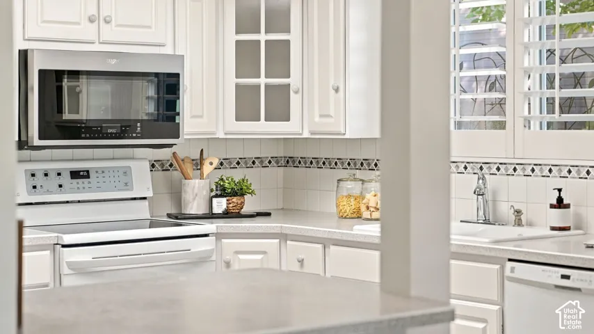 White cabinetry, stainless steel microwave, white electric range, tile backsplash with decorative accents, and white plantation shutters