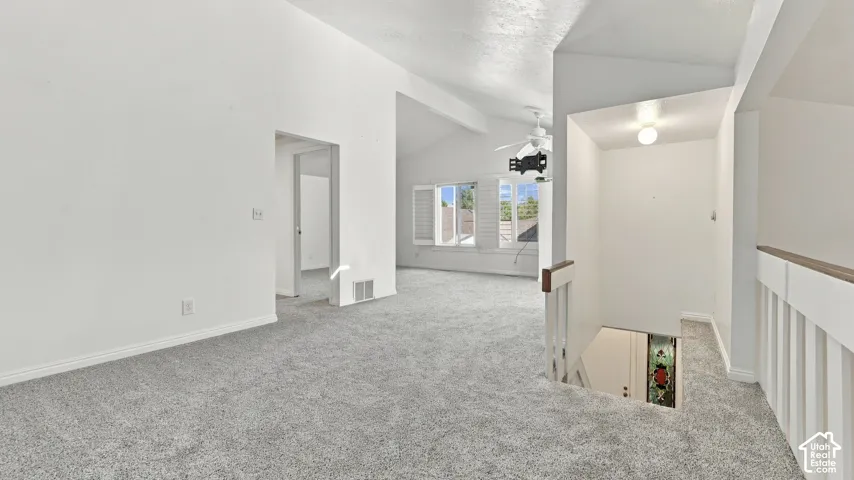 Vaulted ceilings, light gray carpeting, white walls, white window shutters, and a stairwell with white balusters and wood-finish handrails