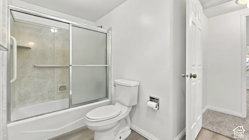 Tub and shower combination with sliding glass doors, white toilet, and wood-finish flooring