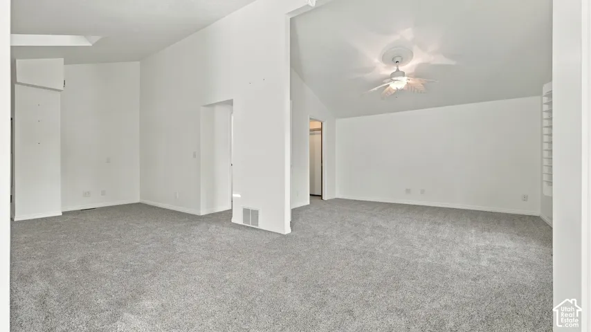 Spacious room with vaulted ceilings, neutral-toned carpet, ceiling fan with integrated lighting, and a skylight