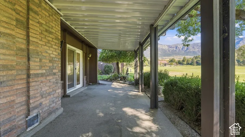 Expansive covered patio featuring a concrete surface, brick exterior wall, sliding glass door access, and distant mountain scenery