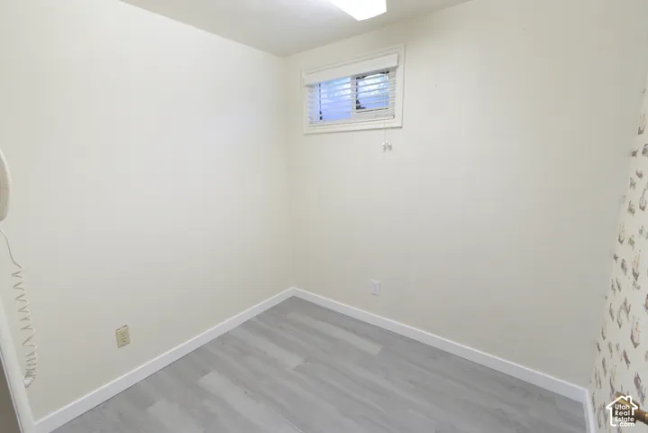 Light wood-finish flooring with white baseboards, a single window with blinds, and flush-mount ceiling lighting