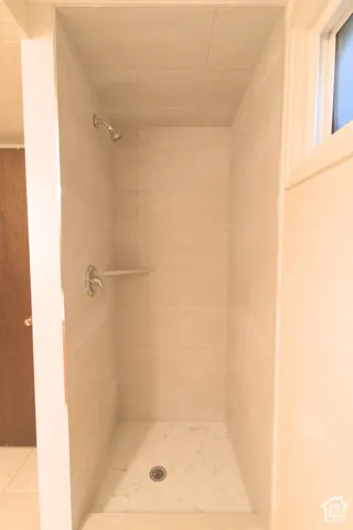 Fully tiled shower enclosure with light-toned wall tiles, a corner shelf, and a mosaic tile floor