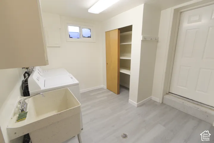 Laundry area featuring a utility sink with a chrome faucet, light wood-finish flooring, and a built-in storage closet with shelving