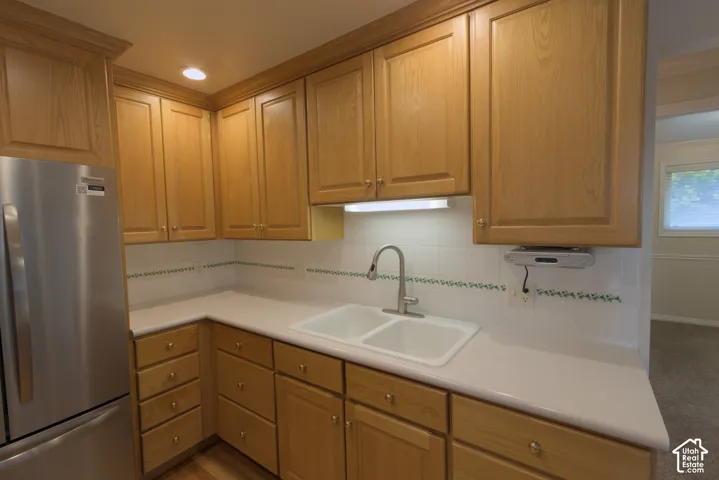 Full height wood-finish cabinetry with crown molding, solid surface countertops, dual basin sink with gooseneck faucet, and integrated recessed lighting