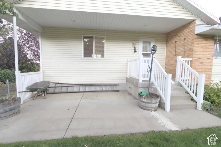 Covered concrete patio featuring white railing and a side entrance with a white door