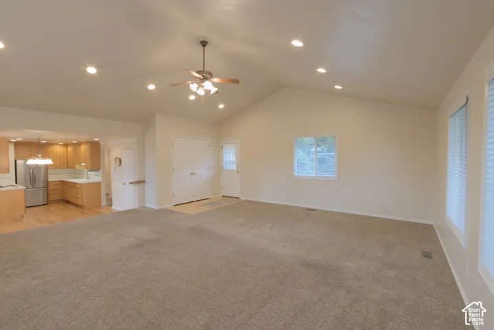 Vaulted ceilings, recessed lighting, ceiling fan, white paneled double doors, and multiple windows with blinds