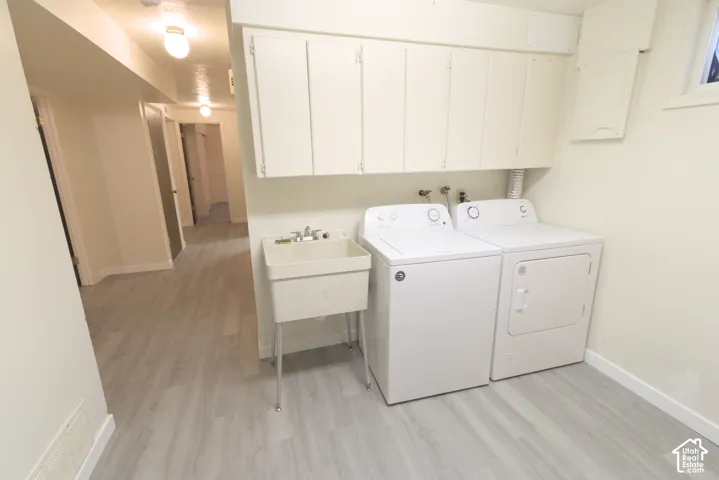 Laundry area featuring a utility sink, white upper cabinetry, and light wood-finish flooring