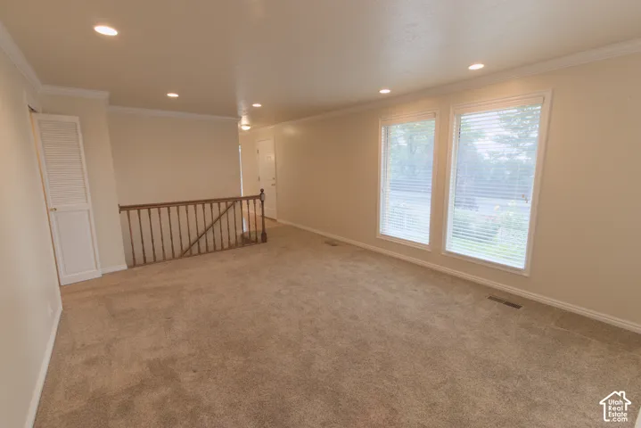 Recessed lighting, crown molding, double windows with blinds, wood railing, and neutral carpet