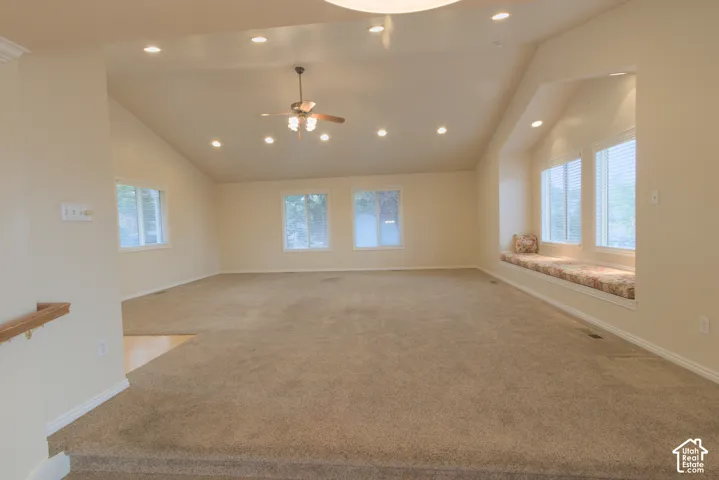 Vaulted ceiling with recessed lighting and a ceiling fan, carpeted flooring, multiple windows, and a built-in window bench