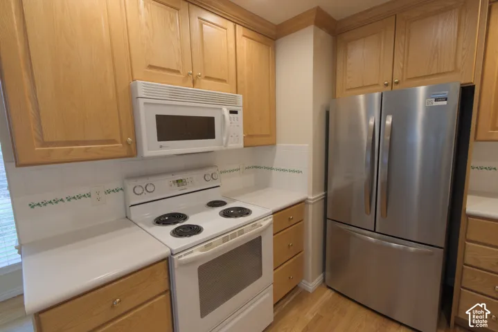 Kitchen featuring light wood-finish cabinetry, white countertops, a white electric range, a white over-the-range microwave, and a stainless steel French door refrigerator