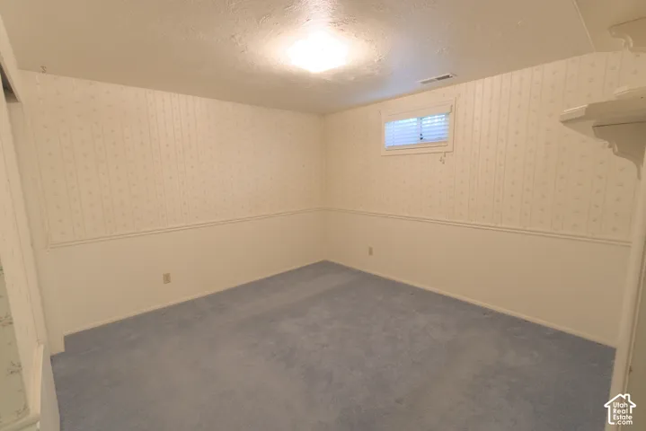 Recessed window with horizontal blinds, patterned wallpaper, wall paneling, and blue carpeting