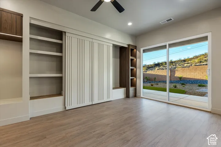Wood-finish flooring, built-in shelving, integrated lighting, sliding glass door, and a ceiling fan