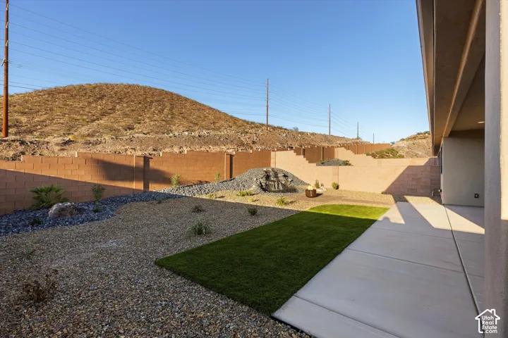 Expansive backyard featuring a concrete patio, artificial turf area, and decorative rock landscaping with a water feature