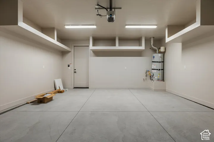 Spacious garage featuring a concrete floor, built-in overhead shelving, two linear fluorescent light fixtures, and a water heater installation