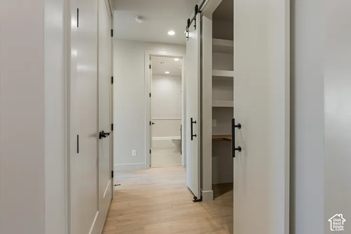 Light wood-finish flooring, white solid core doors with black hardware, recessed lighting, white square tile tub surround, and a barn door with integrated shelving
