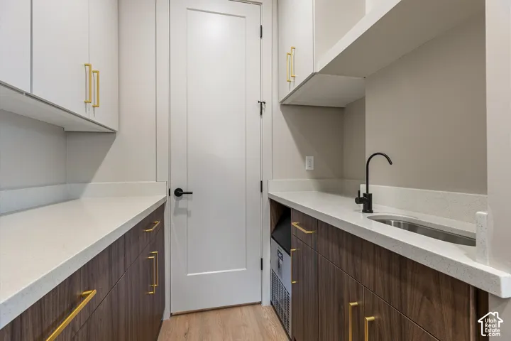 Built-in cabinetry with gold-finish hardware, light-toned countertops, integrated sink with matte black faucet, and wood-finish flooring